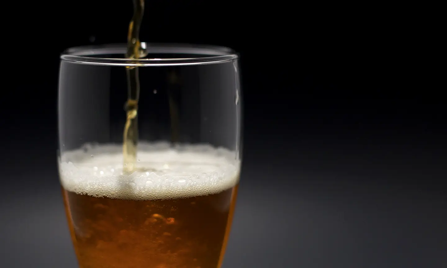 Beer being poured into an unbranded glass against a dark background.