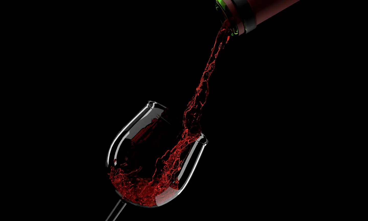 Red wine being poured into a stemmed glass against black.