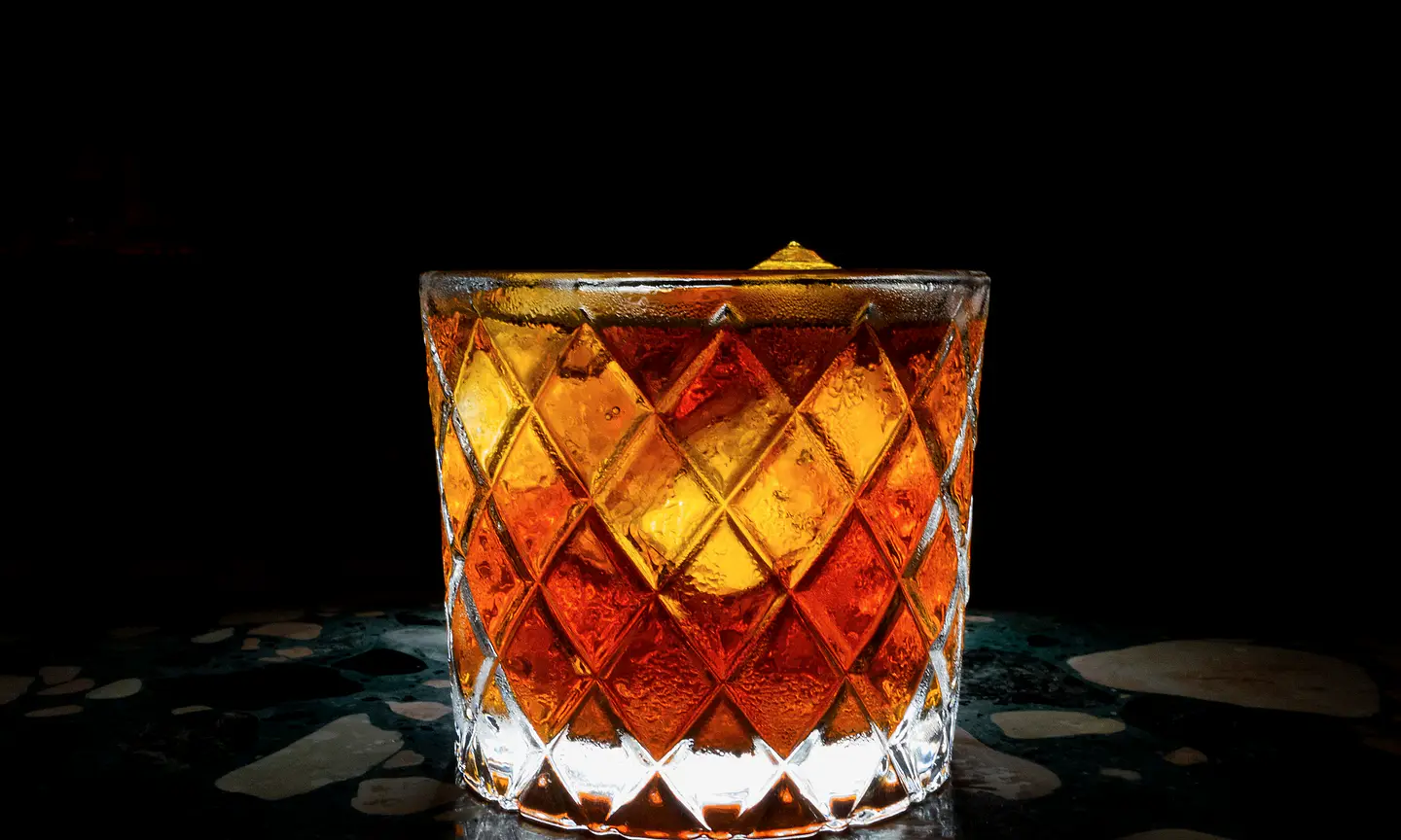 Amber cocktail in a crystal glass against black.