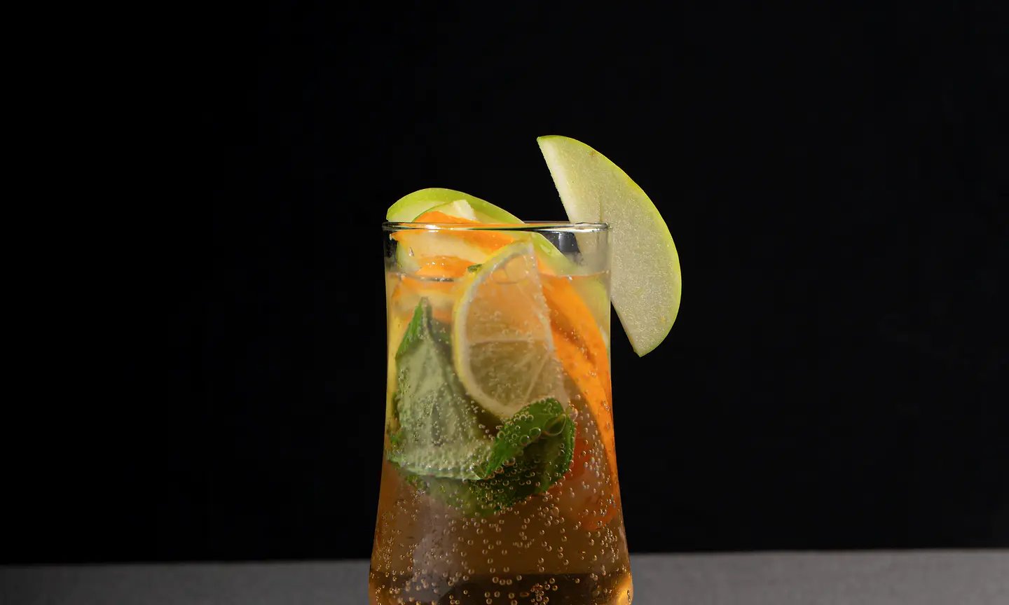 Clear cocktail with lemon and herbs on a dark background.