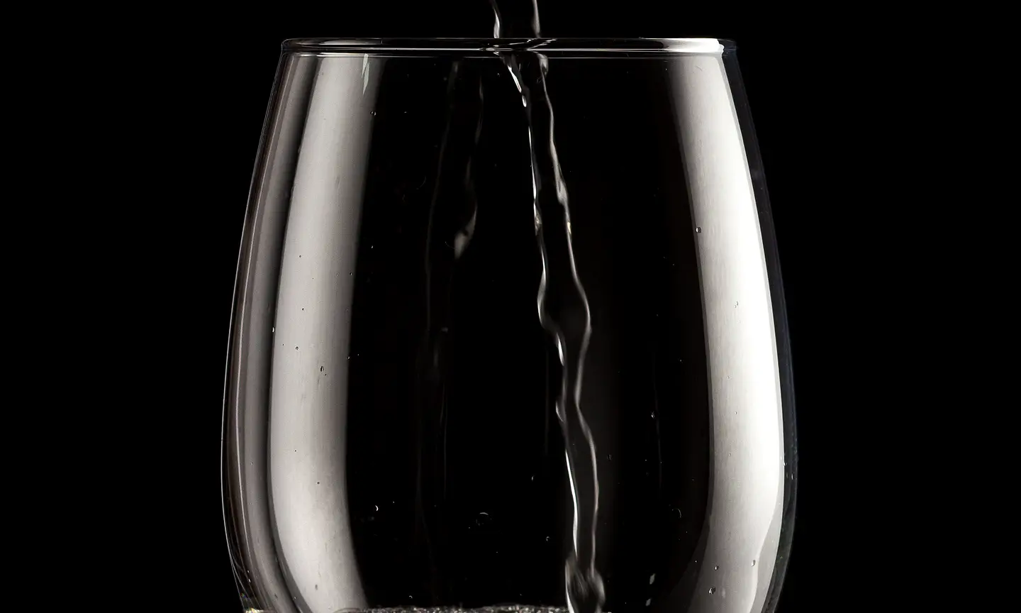 White wine being poured into a stemmed glass against black.