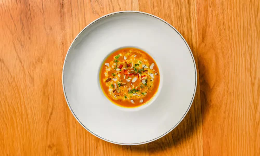 Murgh Badam Shorba served in a shallow blue-gray bowl.
