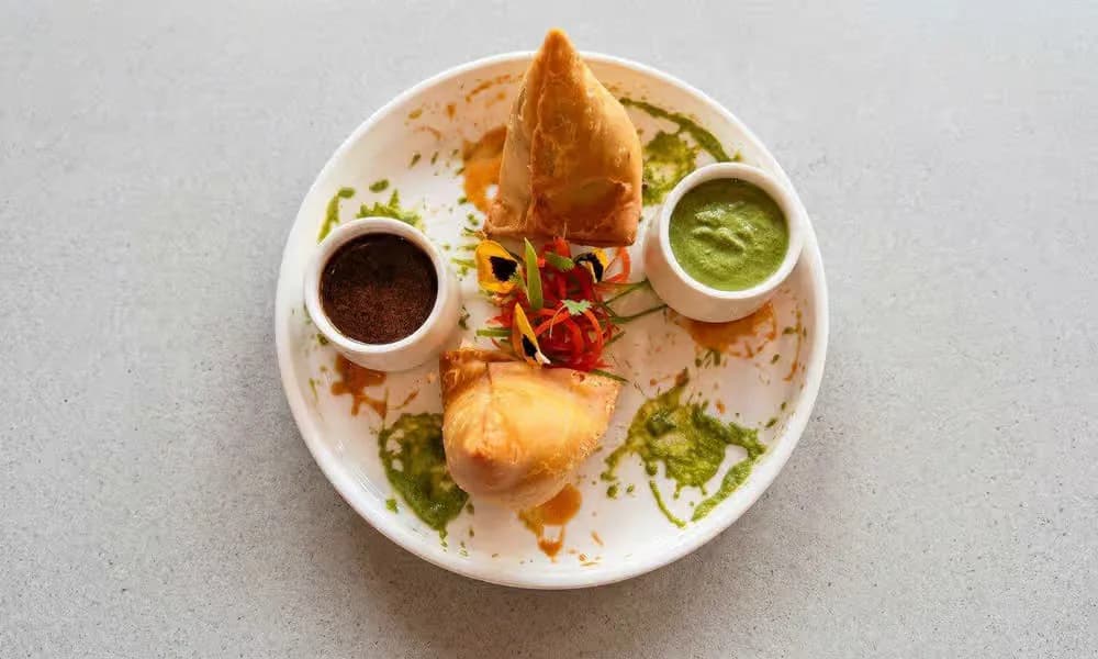 Punjabi Samosa served with chutneys on a white plate.
