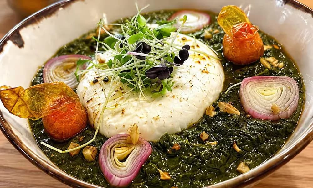 Saag Burrata presented with greens and roasted vegetables.