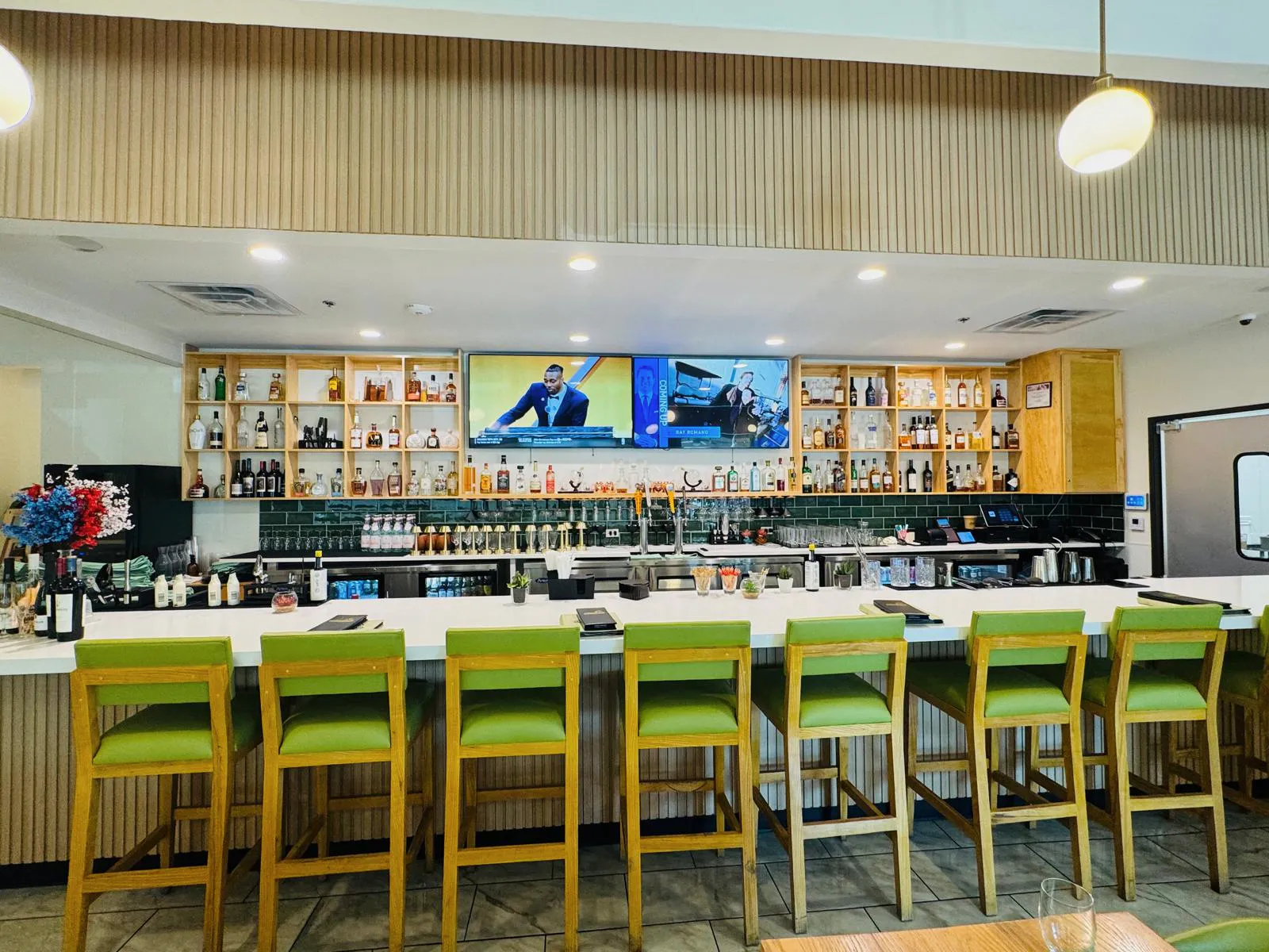 Bar at Namak with green counter seating, warm wood shelving, and a white stone counter.