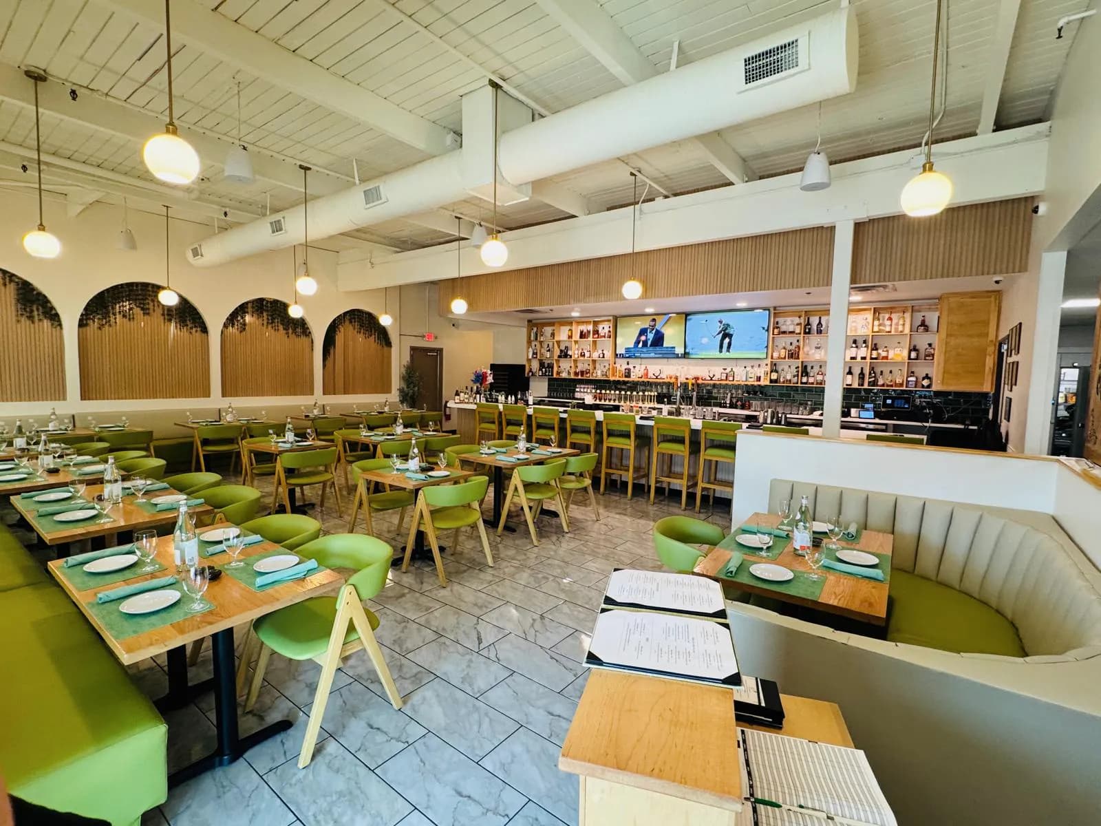 Dining room at Namak with green chairs, set tables, pendant lighting, and the bar beyond.