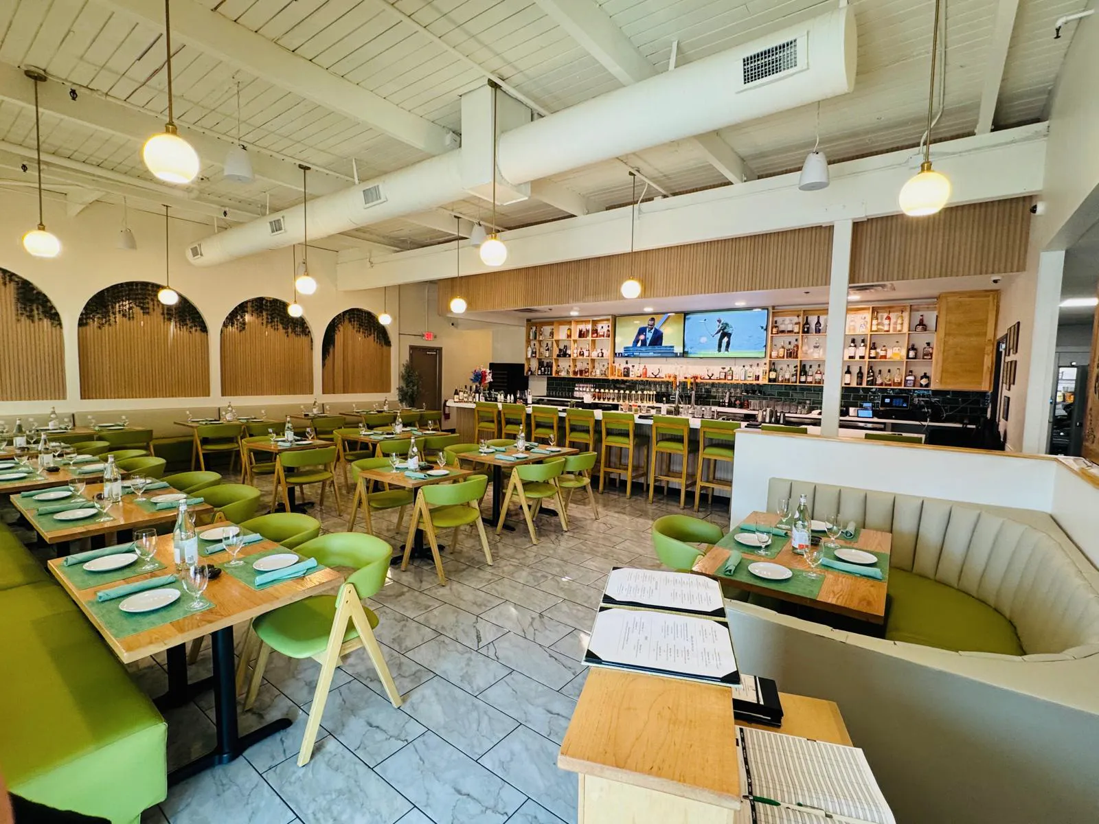 Dining room at Namak with green chairs, set tables, pendant lighting, and the bar beyond.