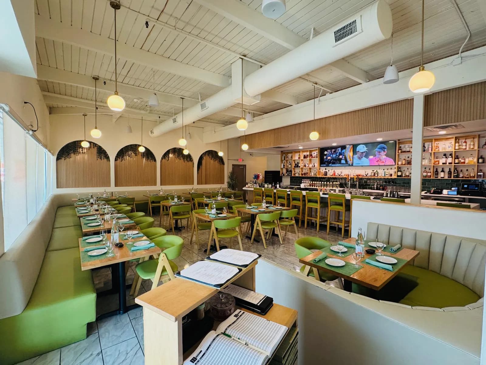 Dining room at Namak with green seating, warm pendant lights, and the bar in the background.