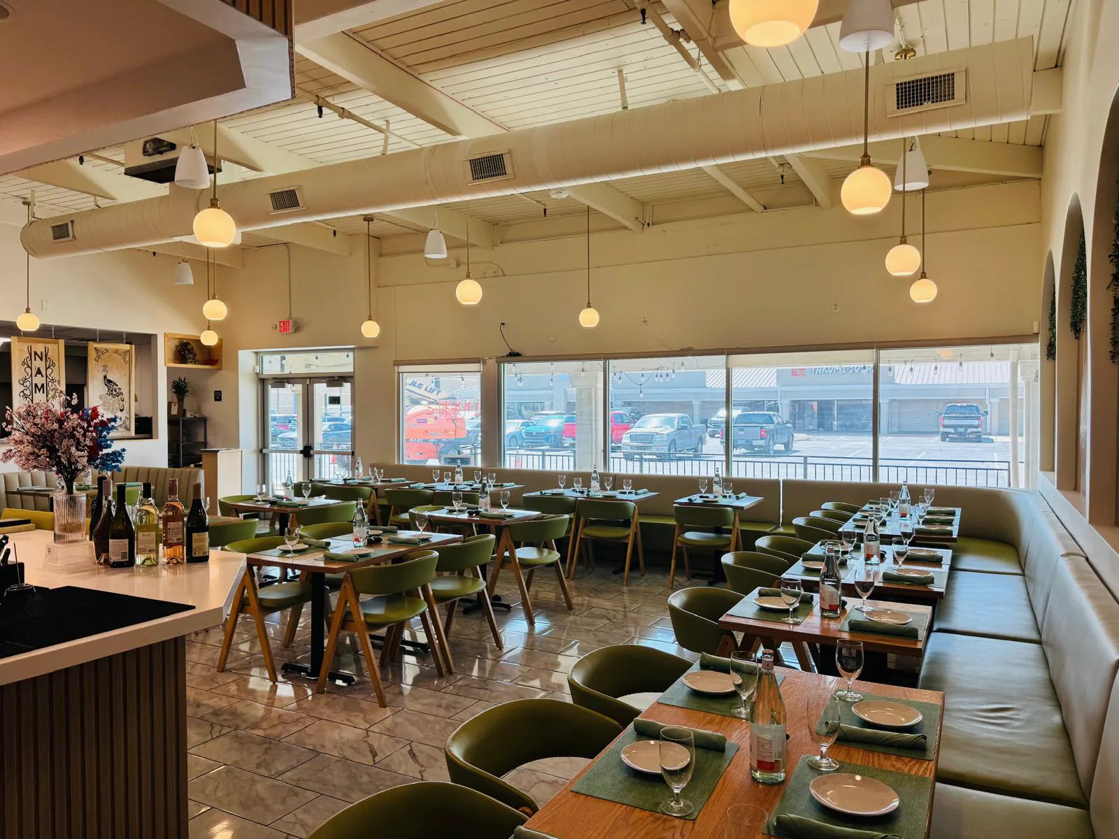 Daylit Namak dining room with green seating, set tables, and pendant lights.